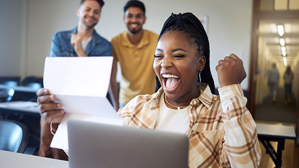 A women is looking at the paper and laptop and cheering and also there are two boys and both of them are happy